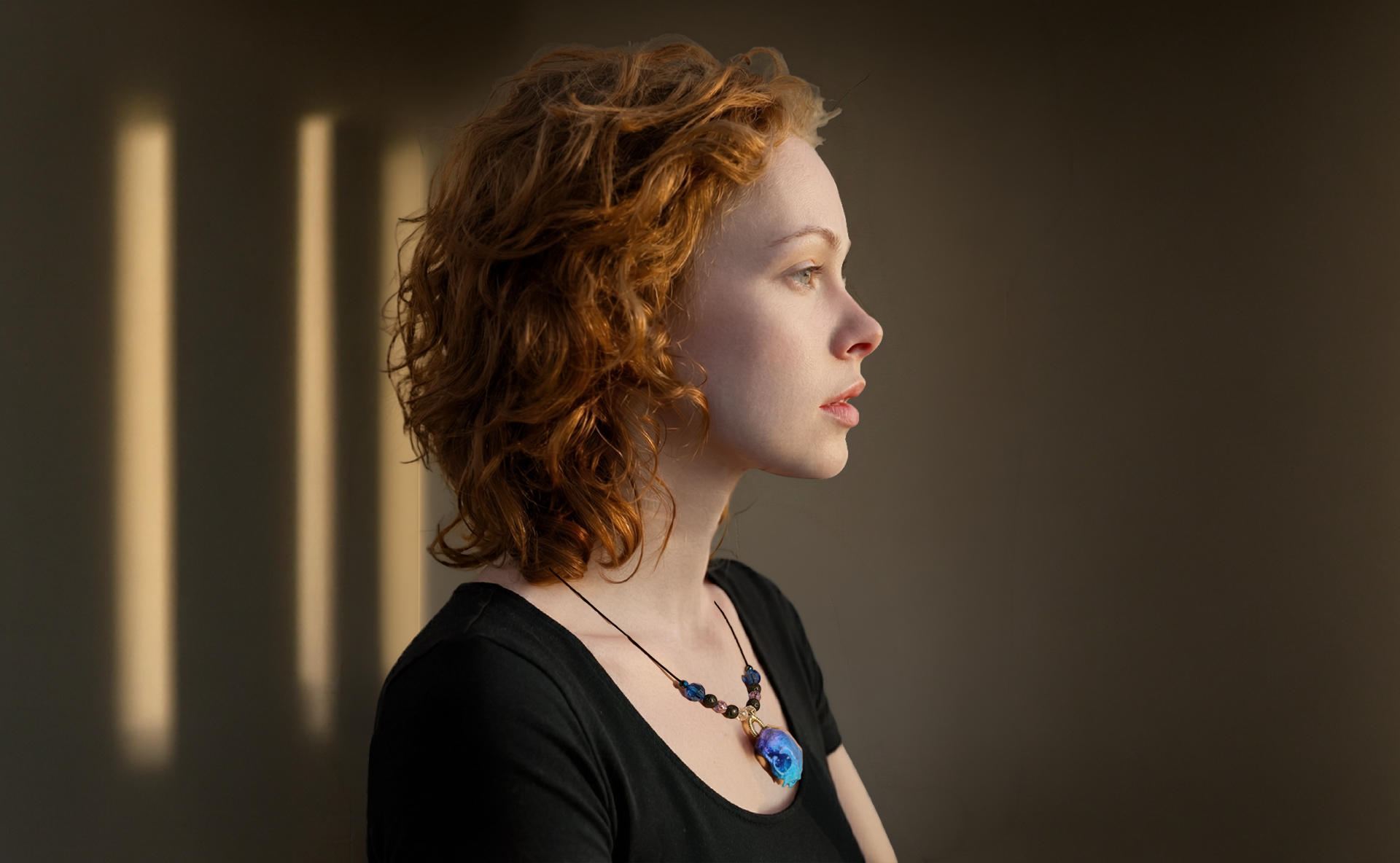 Woman with red hair and a black top against a dark background with vertical light bars.